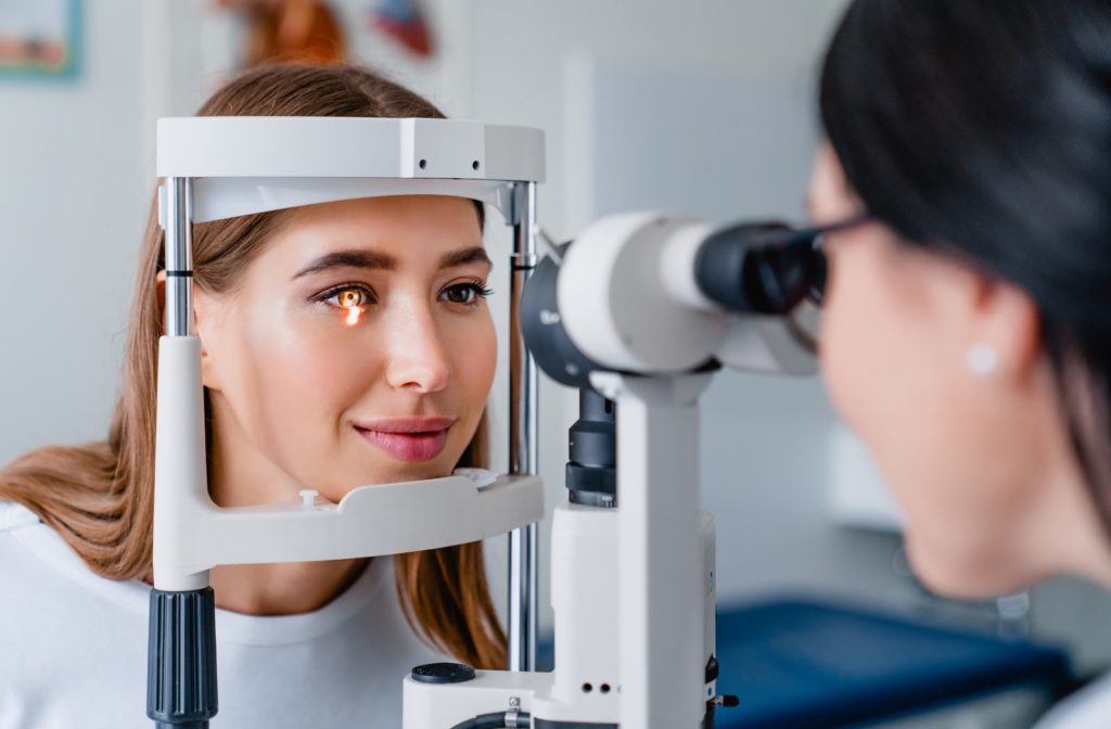 Young woman undergoing eye exam with light focusing on to her eye by her optometrist.